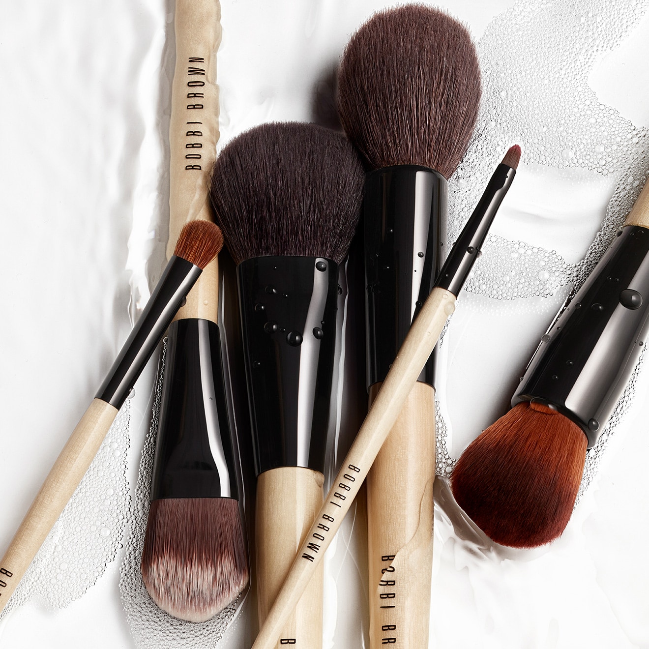 Selection of bestselling Bobbi Brown makeup brushes nesting in bubbly water