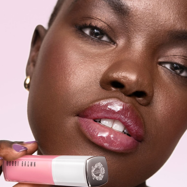 Model holding Extra Plump Lip Serum in front of a pink background